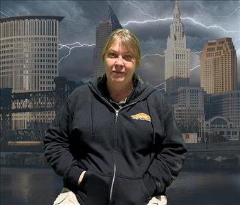 Picture of a blonde woman in a black zip up hoodie in front of a picture of Cleveland during a storm
